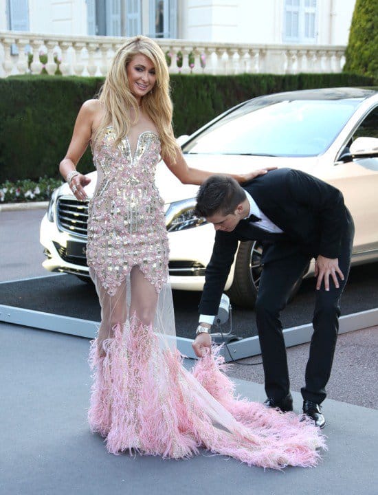 Paris Hilton smiling at photographers as boyfriend River Viiperi fixes the skirt of her gown