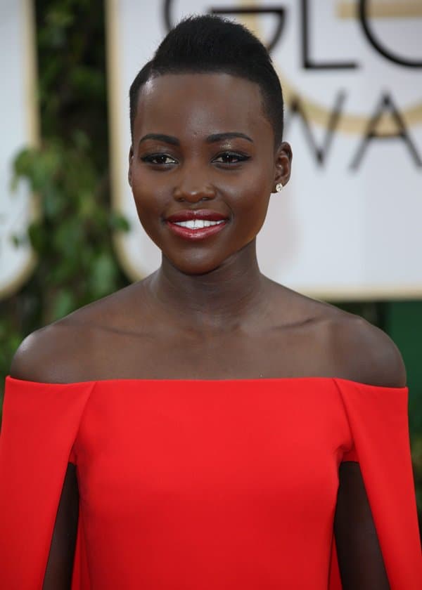 Lupita Nyong'o in a lipstick red silk crepe gown featuring an off-the-shoulder neckline and a "cape" detail framing