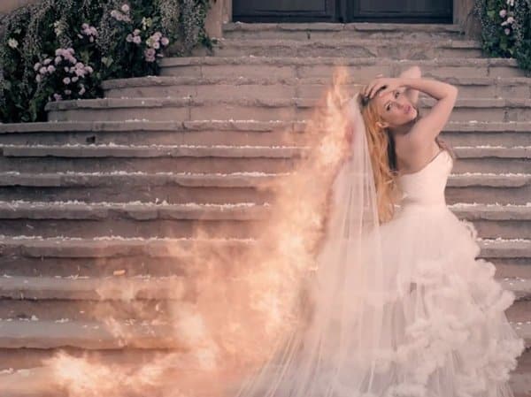 Standing on the church steps, the ruffled train of Shakira's wedding dress catches fire in the music video for Empire