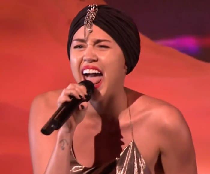 Miley Cyrus sang her popular tune "Wrecking Ball" on The X Factor UK, sporting a black turban from Brick Lane Street and a shiny, full-length gold dress designed by Marc Jacobs
