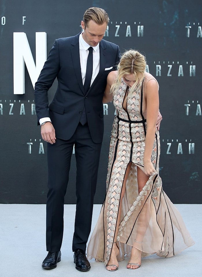 Margot Robbie bends over to fix her shoes causing her dress to unzip