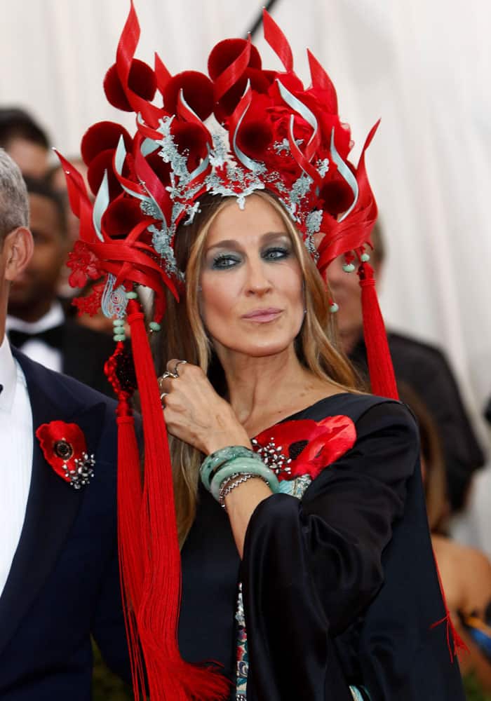 Sarah Jessica Parker in a wild Philip Treacy headpiece with long tassels, ribbony flames, and a load of furry, red pom-poms at the MET Gala 2015