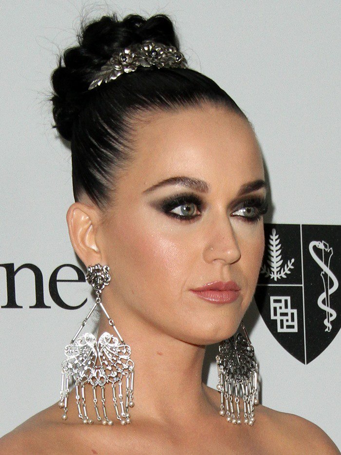 Katy Perry added a touch of sophistication to her elegant ensemble by complementing it with a pair of exquisite silver chandelier earrings and a matching tiara, which gracefully held her black tresses in place