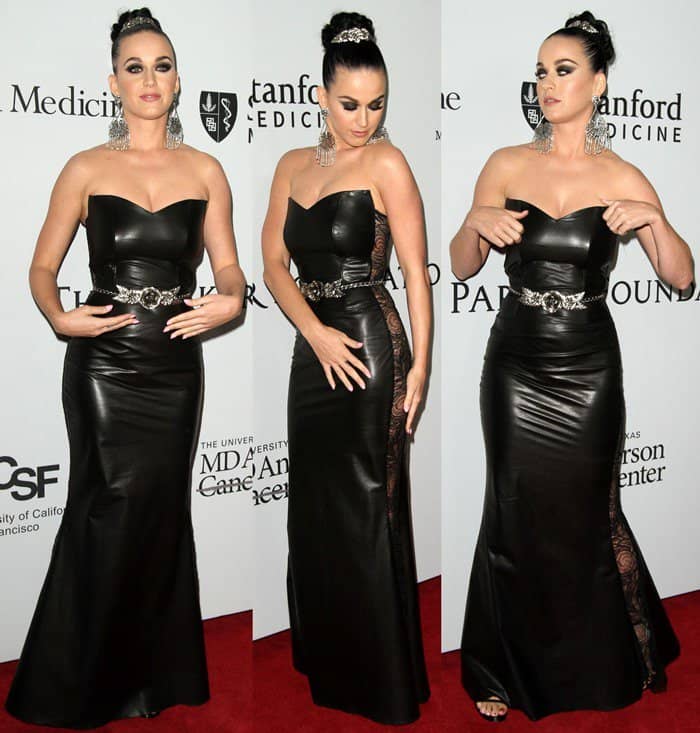 Katy Perry donning a striking strapless black Deborah Drucker Spring 2015 leather gown featuring exposed lace panels and a statement belt, complemented by a high bun, smokey eyes, and elegant Chandelier drop earrings